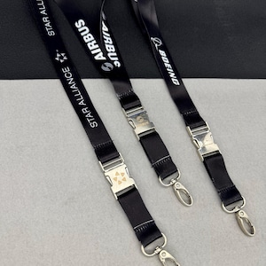 May include: Three black lanyards featuring white printed text and logos. One displays Star Alliance, one displays Airbus, and one displays Boeing. Each lanyard includes a silver-toned metal side-release buckle and a silver metal lobster clasp.