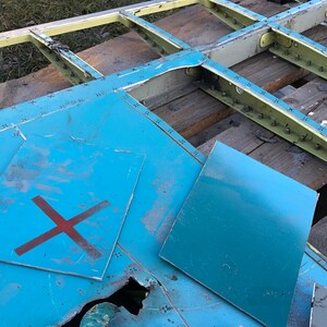 May include: Two blue metal panels with a red X painted on one panel. The panels are lying on a wooden surface with a metal frame.