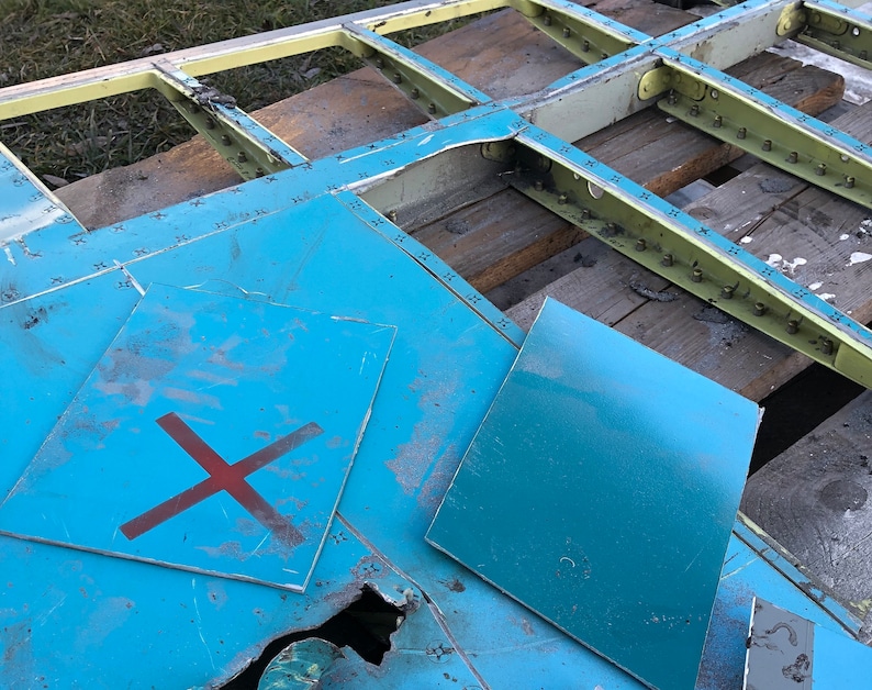 May include: Two blue metal panels with a red X painted on one panel. The panels are lying on a wooden surface with a metal frame.