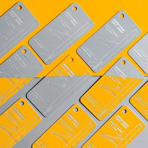 May include: A collection of rectangular luggage tags featuring a Boeing 757-300 aircraft outline. The tags are colored in either solid gray or solid yellow, each with a circular hole at the top and printed text including Reg. D-ABOE L/N 849.