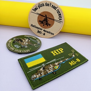 May include: Three embroidered patches featuring a helicopter design. The first patch is beige with brown text that reads "Real pilots don't need runways" and "Helicopter squadron Mi-8". The second patch is green with yellow text that reads "HIP Mi-8". The third patch is beige with brown text that reads "Повітряні Сили" and "Keep calm and save lives".