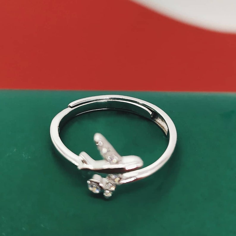 Op de afbeelding: Een zilveren ring met een klein vliegtuigontwerp versierd met heldere strass.