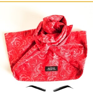 May include: A red satin hair scarf with a floral pattern and the text "GLITCHA - HANDMADE IN ITALY" on a white background. The scarf is folded into a turban shape. Below the scarf are two stylized eyes with long eyelashes.