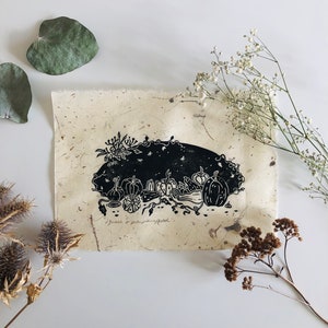 Op de afbeelding: Zwart-witte linosnede op gestructureerd papier met een stilleven van pompoenen en pompoenen met de tekst "squash & pumpkin patch".