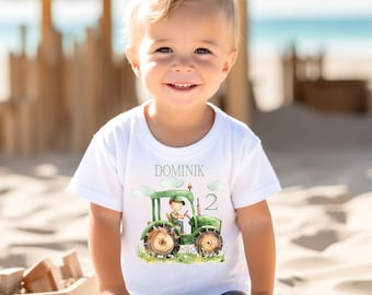 May include: White t-shirt with a green tractor and a boy driving it. The shirt says "Dominik" and "2" on it.