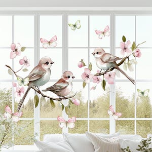 Op de afbeelding: Een raam met uitzicht op een bos, versierd met roze en witte bloemendecals en drie kleine vogels. De vogels zitten op takken met roze bloemen. Vlinders zijn ook in het ontwerp opgenomen.