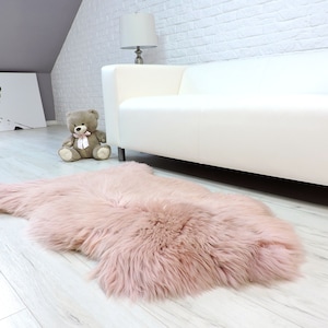Könnte beinhalten: Ein weicher, rosa Kunstfellteppich mit langen, flauschigen Fasern. Der Teppich liegt auf einem hellen Holzboden in einem Raum mit einem weißen Sofa und einem Teddybären.