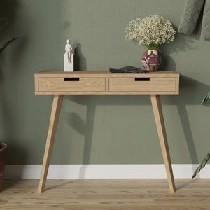 May include: A light wood console table with two drawers and tapered legs. The table is decorated with a small white figurine, a vase of white flowers, and a pair of black gloves.
