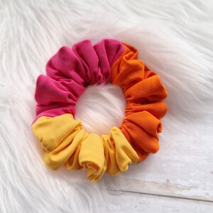 Pode incluir: Um scrunchie de tecido rosa, laranja e amarelo.