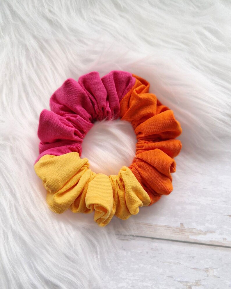 Pode incluir: Um scrunchie de tecido rosa, laranja e amarelo.