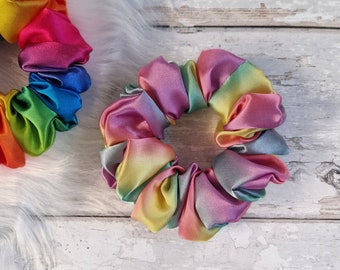 May include: Two rainbow-colored satin scrunchies. One is a bright rainbow with red, orange, yellow, green, blue, indigo, and violet. The other is a pastel rainbow with pink, purple, blue, green, yellow, and orange.