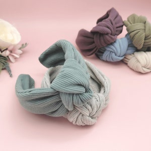 May include: A set of five fabric headbands in different colours, including light blue, grey, purple, and green. The headbands are made of a soft, stretchy fabric and have a knotted design.