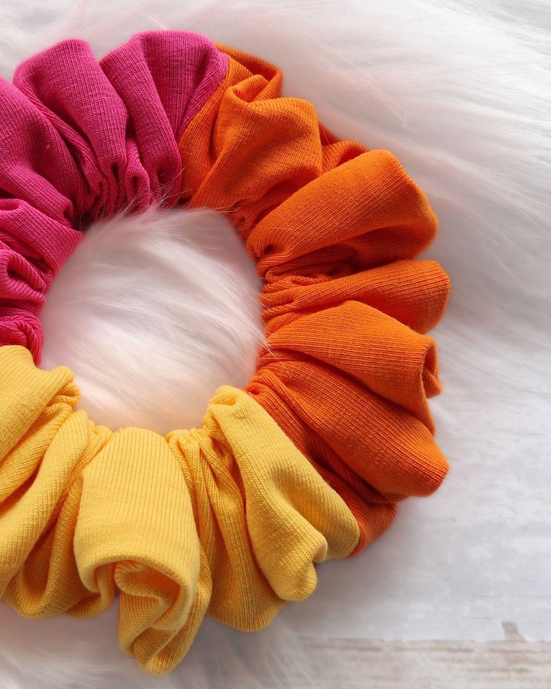 Pode incluir: Um scrunchie para cabelo colorido feito de tecido em tons de rosa, laranja e amarelo. O scrunchie &eacute; feito de tecido macio e el&aacute;stico, perfeito para segurar o cabelo no lugar.