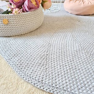 May include: A gray crocheted round rug with a basket of pink flowers in the background.
