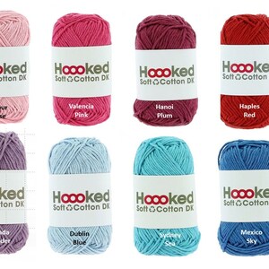 Può includere: Otto gomitoli di lana in diversi colori, tra cui rosa, rosso, viola, blu e verde. Ogni gomitolo ha un'etichetta bianca con il testo "Hoooked Soft Cotton DK" e il nome del colore.