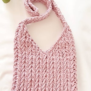 Puede incluir: Un bolso de hombro de crochet rosa con una correa trenzada. El bolso tiene un peque&ntilde;o bot&oacute;n dorado en la parte inferior.