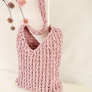 Puede incluir: Una bolsa de mano de crochet rosa con una correa larga. La bolsa tiene un dise&ntilde;o simple y texturizado.