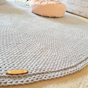 May include: A gray round crocheted rug with a wooden tag that says "EMRINOELLE handmade with love".