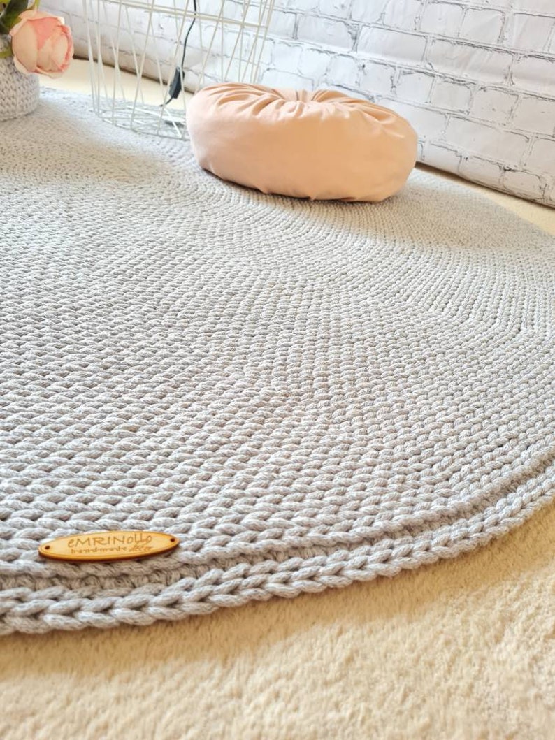 May include: A gray round crocheted rug with a wooden tag that says "EMRINOELLE handmade with love".