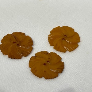 Pode incluir: Três botões de plástico castanho com um desenho de flor. Cada botão tem dois furos.