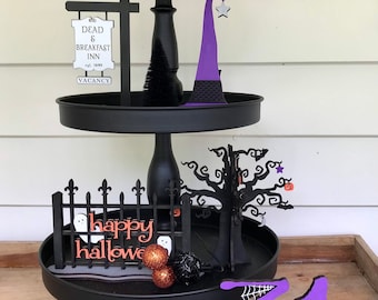 Könnte beinhalten: Ein dreistufiges schwarzes Tablett mit Halloween-Dekorationen. Die oberste Ebene hat ein "BOO"-Schild und einen orangefarbenen Baum. Die mittlere Ebene hat ein "Dead & Breakfast Inn"-Schild und einen Hexenhut. Die untere Ebene hat einen Zaun mit dem Text "happy halloween" und einen Baum.