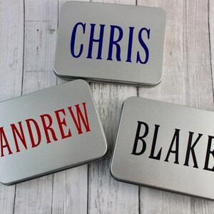 May include: Three silver metal boxes with personalized names. The names are "Chris", "Andrew", and "Blake". The names are printed in different colors on each box.