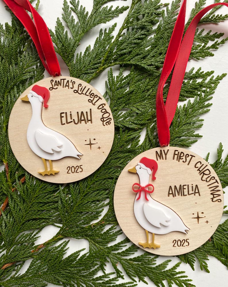 May include: Two wooden Christmas ornaments with red ribbon hangers. Each ornament features a white goose wearing a Santa hat. One says "Santa's Littlest Goose" and "Elijah 2025". The other says "My First Christmas" and "Amelia 2025".
