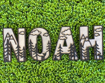 May include: Wooden letters spelling the name "NOAH" with a nature-themed design. Each letter features a mountain range, clouds, and pine trees.