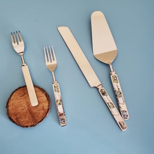 May include: Four pieces of cutlery with decorative handles. The handles are made of mother of pearl and have a floral design. The cutlery includes a fork, a knife, and two spoons.