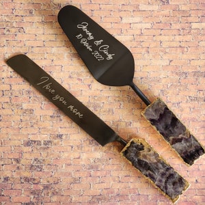 May include: Black cake cutting set with amethyst handles. The server is engraved with "Jenny & Cindy 10 October 2022" and the knife is engraved with "I love you more".