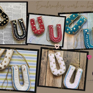 May include: A set of six embroidered felt letter U ornaments in various colors, including black, red, teal, white, and pink. Each ornament features a gold trim and is decorated with sequins and beads. The ornaments are hung on a string and the text "Embroidery work on both sides" is visible in the image.