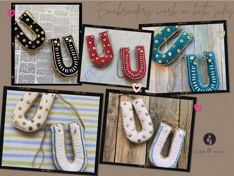 May include: A set of six embroidered felt letter U ornaments in various colors, including black, red, teal, white, and pink. Each ornament features a gold trim and is decorated with sequins and beads. The ornaments are hung on a string and the text "Embroidery work on both sides" is visible in the image.