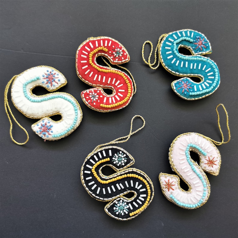 May include: Five felt ornaments shaped like the letter S, each decorated with colorful beads and sequins. The ornaments are in red, white, black, pink, and blue.