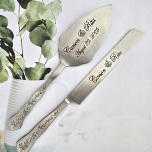 May include: A silver cake server and knife set. The server has a leaf-shaped blade with the names "Carson & Rita" and the date "August 29, 2026" engraved. Both pieces have decorative leaf patterns on the handles.