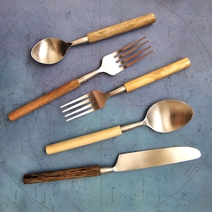 May include: A set of four silver utensils with wooden handles. The utensils include a fork, a spoon, a knife, and a smaller fork. The utensils are arranged on a blue background with a star pattern.