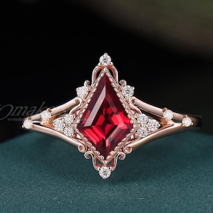 Könnte beinhalten: Ein roségoldener Ring mit einem großen, leuchtend roten Edelstein in Drachenform, umgeben von kleineren, klaren Akzentsteinen. Der Ring hat ein verziertes Filigran-Design mit filigranen Details und einer polierten Oberfläche. Der Ring ist vor einem dunklen Hintergrund platziert.