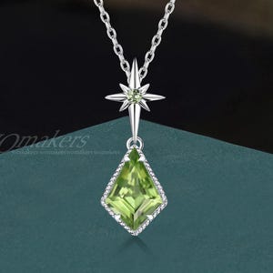 May include: A silver necklace with a starburst pendant and a green, square-cut gemstone. The gemstone is set within a diamond-shaped frame with small, clear stones. The necklace chain is delicate and silver.