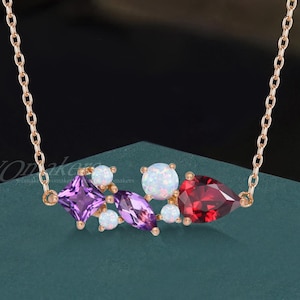May include: A rose gold necklace featuring a cluster of gemstones. The necklace has a delicate chain and a pendant with a purple square, a red pear-shaped stone, white opals, and purple marquise-cut stones.