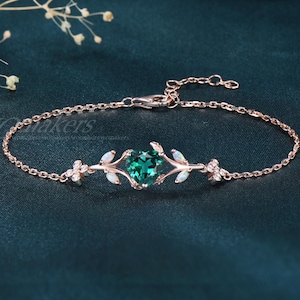 May include: Rose gold bracelet featuring a heart-shaped emerald green gemstone. The bracelet has delicate floral and leaf accents with small white gemstones. The chain is fine and adjustable, perfect for a special occasion.