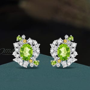 May include: A pair of silver earrings with a green oval gemstone surrounded by smaller white and yellow gemstones.