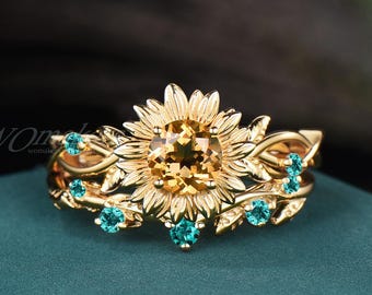 Könnte beinhalten: Ein goldener Ring mit einem zentralen, runden, gelben Edelstein in Sonnenblumenform, umgeben von goldenen Blütenblättern und Blättern. Der Ring ist mit kleinen, runden, türkisfarbenen Edelsteinen besetzt, die in die Struktur eingearbeitet sind.