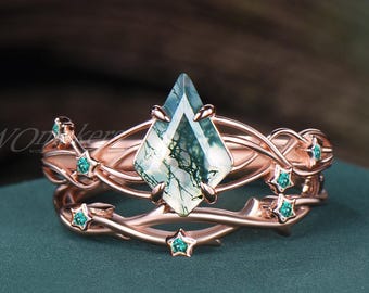 Könnte beinhalten: Roségoldenes Ring-Set mit einem rautenförmigen Moosachat-Edelstein. Der Ring ist mit kleinen, teal-farbenen sternförmigen Edelsteinen und weinrebenartigen Details verziert. Das Set enthält ein passendes Band mit ähnlichen Designelementen.