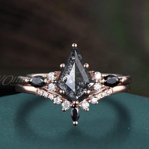 May include: A rose gold engagement ring set with a kite-shaped, salt and pepper diamond center stone. The ring is accented with small white and black gemstones. The band features a delicate design, perfect for a wedding or anniversary.