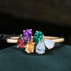 Peut inclure: Une bague en or ornée d'un groupe de pierres précieuses en forme de poire de différentes couleurs. Les pierres précieuses comprennent le rouge, le violet, le jaune, le vert, le bleu clair et le blanc. La bague a un anneau fin.