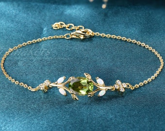 May include: A gold chain bracelet with a green gemstone and white opal accents. The bracelet features a delicate leaf design.