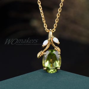 May include: A gold necklace with a green gemstone pendant. The pendant is shaped like a leaf with two white opal stones on the stem.