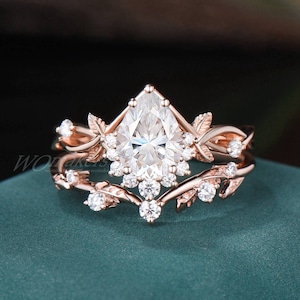 May include: A pear-shaped diamond engagement ring set with a delicate, leafy design in rose gold. The ring features a large centre stone surrounded by smaller diamonds and intricate leaf details.
