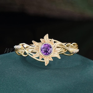 Könnte beinhalten: Ein goldener Ring mit einem violetten Edelstein, der in einem Sonnenmotiv gefasst ist. Der Ringband ist ein zartes, gedrehtes Rankendesign.