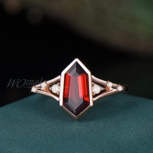 May include: A rose gold ring with a large, red, octagonal gemstone surrounded by smaller, clear gemstones.