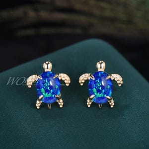 Könnte beinhalten: Ein Paar goldfarbene Ohrringe mit einem blauen Opal-Schildkröten-Design.